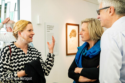 Drei Menschen unterhalten sich in einer Ausstellung, Sylvie Ahrens-Urbanek erklärt den beiden anderen etwas.