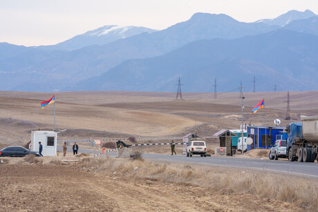 Ein einfach, leerer Grenzübergang in einer kargen Landschaft vor dem nur wenige Fahrzeuge warten. Im Hintergrund ist eine Bergkette sichtbar.