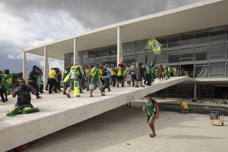 Menschen mit brasilianischen Flaggen marschieren durch eine geöffnete Fensterscheibe in das brasilianische Nationalkongressgebäude