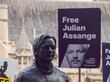 Statue von Julian Assange auf einem Protest in England mit Schild wo drauf steht "Free Julian Assange"