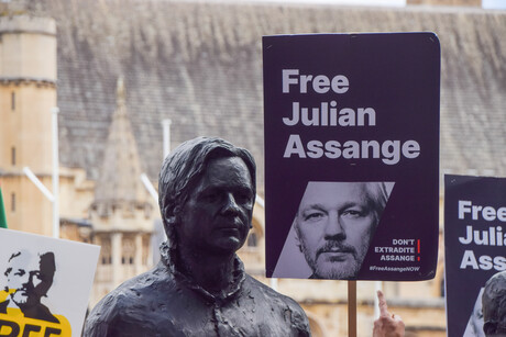 Statue von Julian Assange auf einem Protest in England mit Schild wo drauf steht "Free Julian Assange"