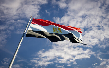 Die Nationalflagge Ägyptens (erst ein roter, dann ein weißer und zuletzt ein schwarzer Querstreifen; auf dem weißen Streifen ist mittig ein goldener Adler zu sehen) weht vor dme Himmel