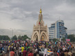 Menschen drängen sich um ein cremefarbenes Monument; im Hintergrund steht ein Hochhaus