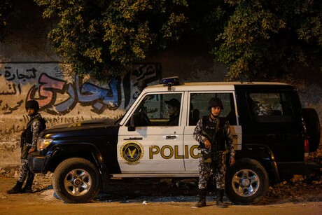 Ägyptische Polizeikräfte stehen vor einem schwarz-weißem Polizeifahrzeug, dass wiederum vor einer mit Graffiti besprühten Wand steht