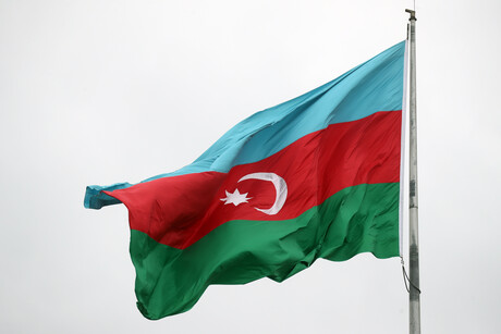 Die Nationalflagge Aserbaidschans (erst ein hellblauer, dann ein roter und zuletzt ein dunkelgrüner Querbalken; auf dem roten Balken sind außerdem ein Halbmond und ein Stern abgebildet) weht vor einem wolkenverhangenen Himmel
