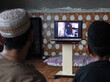 Eine afghanische TV-Moderatorin ist auf einem Fernsehbildschirm zu sehen, zwei Männer betrachten den Bildschirm.