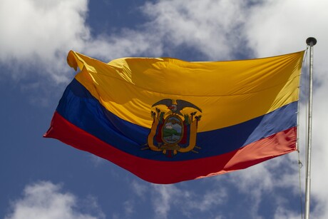 Die Nationalflagge Ecuadors weht vor einem freundlichen Himmel