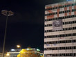 Vor einem dunklen Abendhimmel ist ein Gebäude zu sehen, an dessen Außenfront ein Banner mit dem Gesicht von Khaled Drareni hängt