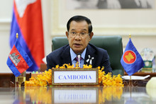 Premierminister Hun Sen hält im sitzen eine Anpsrache; vor ihm auf dem Tisch ist ein Schild mit der Aufschrift "Cambodia" und zwei kleine Flaggen aufgestellt