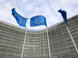 Drei Flaggen der EU wehen an langen Fahnenstangen vor dem Gebäude der Europäischen Kommission