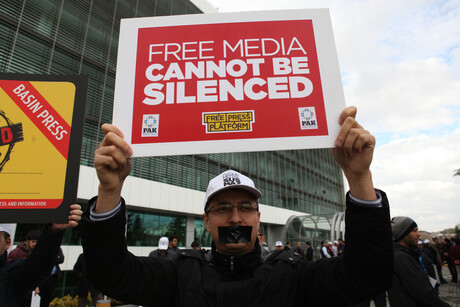 Ein Mann hält ein Schild hoch auf dem steht:"Free media cannot be silenced"