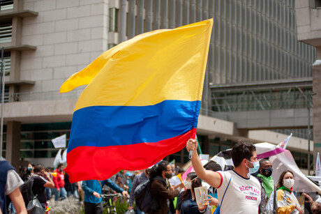 Zahlreiche Demonstrierende; einer von ihnen hält die kolumbianische Nationalflagge hoch