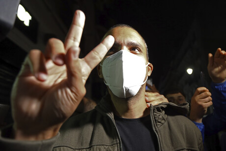 Ein Mann mit Maske formt ein V mit Zeige- und Mittelfinger.