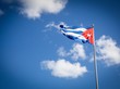 Vor einem blauen Himmel mit weißen Wolken weht die kubanische Flagge: blau-weiße Streifen und ein rotes Dreiek auf der rechten Seite, in dessen Mitte ein weißer Stern zu sehen ist