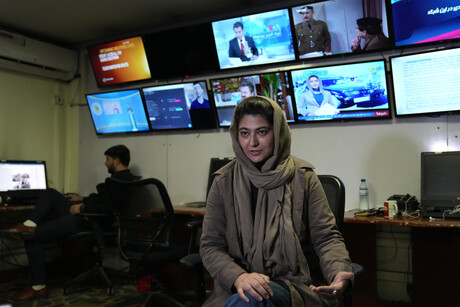 Eine Frau wird in einem Newsroom interviewt. Sie sitzt auf einem Bürostuhl, im Hintergund sind mehrere, an der Wand angebrachte Monitore zu sehen, auf denen diversere Nachrichtenkanäle laufen.