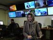 Eine Frau wird in einem Newsroom interviewt. Sie sitzt auf einem Bürostuhl, im Hintergund sind mehrere, an der Wand angebrachte Monitore zu sehen, auf denen diversere Nachrichtenkanäle laufen.