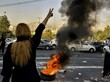 Eine Iranerin zeigt während eines Protests in Teheran das Victory-Zeichen. Vor ihr brennt ein Reifen.