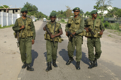 Vier bewaffnete Soldaten gehen eine Straße entlang