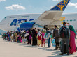 Männer, Frauen und Kinder mit Gepäck, stehen vor einem Flugzeug in einer Schlange