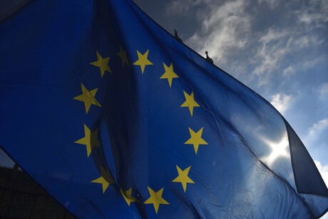 Eine EU Fahne vor blauem Himmel, die Sonne scheint leicht hindurch.