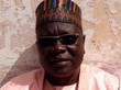Amadou Vamoulké steht mit Sonnenbrille und Kopfbedeckung vor einer cremefarbenen Wand