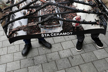Demonstrierende halten ein Schild, auf dem das abgebrannte Haus von Milan Jovanovic zu sehen ist. Unten auf dem Schild ist der Schriftzug "Auf was warten wir?" zu lesen. © picture alliance/AP Photo | Darko Vojinovic