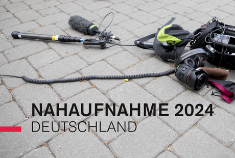 Eine Tonangel, Aufnahmegerät und ein Kameraobjektiv liegen auf einem gepflasterten Boden, darübergelegt steht der Text: Nahaufnahme 2024 Deutschland