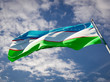 Die Nationalflagge Usbekistans (ein hellblauer Querstreifen mit einigen weißen Sternen und einem weißen Mond auf der linken Seite, darunter ein weißer sowie ein grüner Querstreifen) weht an einer Fahnenstange vor dem blauen Himmel