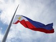 Die Nationalflagge der Philippinen (ein weißes Dreieck an der linken Seite reicht in einen blauen und einen roten Querbalken hinein) weht vor einem leicht wolkenverhangenen Himmel
