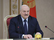 Alexander Lukashenko im Anzug sitz an einem Tisch, vor ihm zwei Mirkofone.