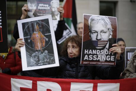 Eine Frau hält während einer Demonstration zwei Bilder hoch: auf dem einen wird auf Assange gezielt, auf dem anderen ist Assange mit der Unterschrift "Hands of Assange - Don't shoot the messenger" zu sehen
