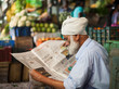 Ein Mann mit weißem Bart und hellem Turban sitzt draußen und liest Zeitung