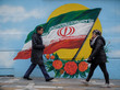 Zwei Personen gehen an einem Gebäude vorbei, auf dessen Mauer die iranische Flagge gemalt wurde
