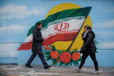 Zwei Personen gehen an einem Gebäude vorbei, auf dessen Mauer die iranische Flagge gemalt wurde